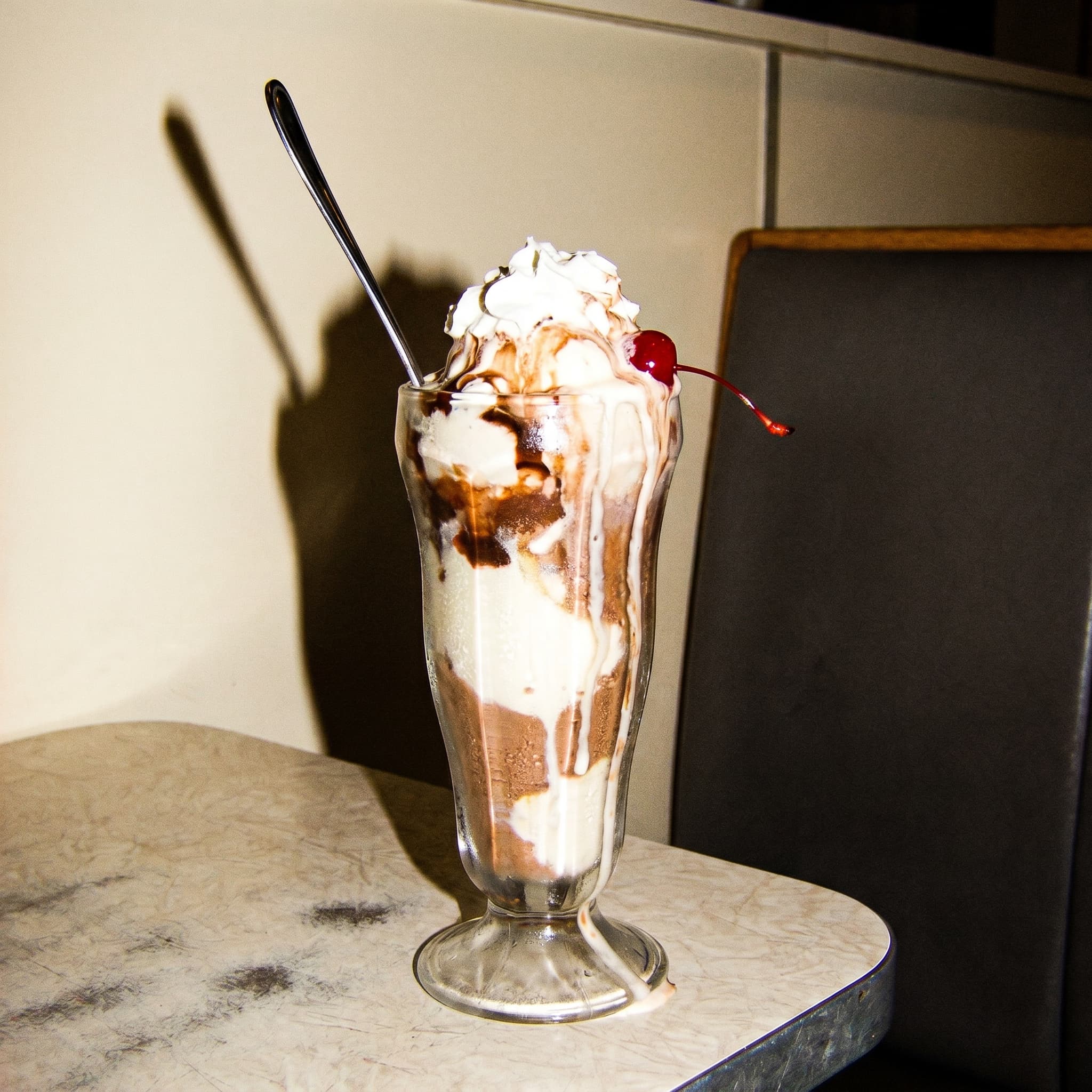 An ice-cream sundae melting fast in a tall glass, drips on the counter, frozen by camera flash.