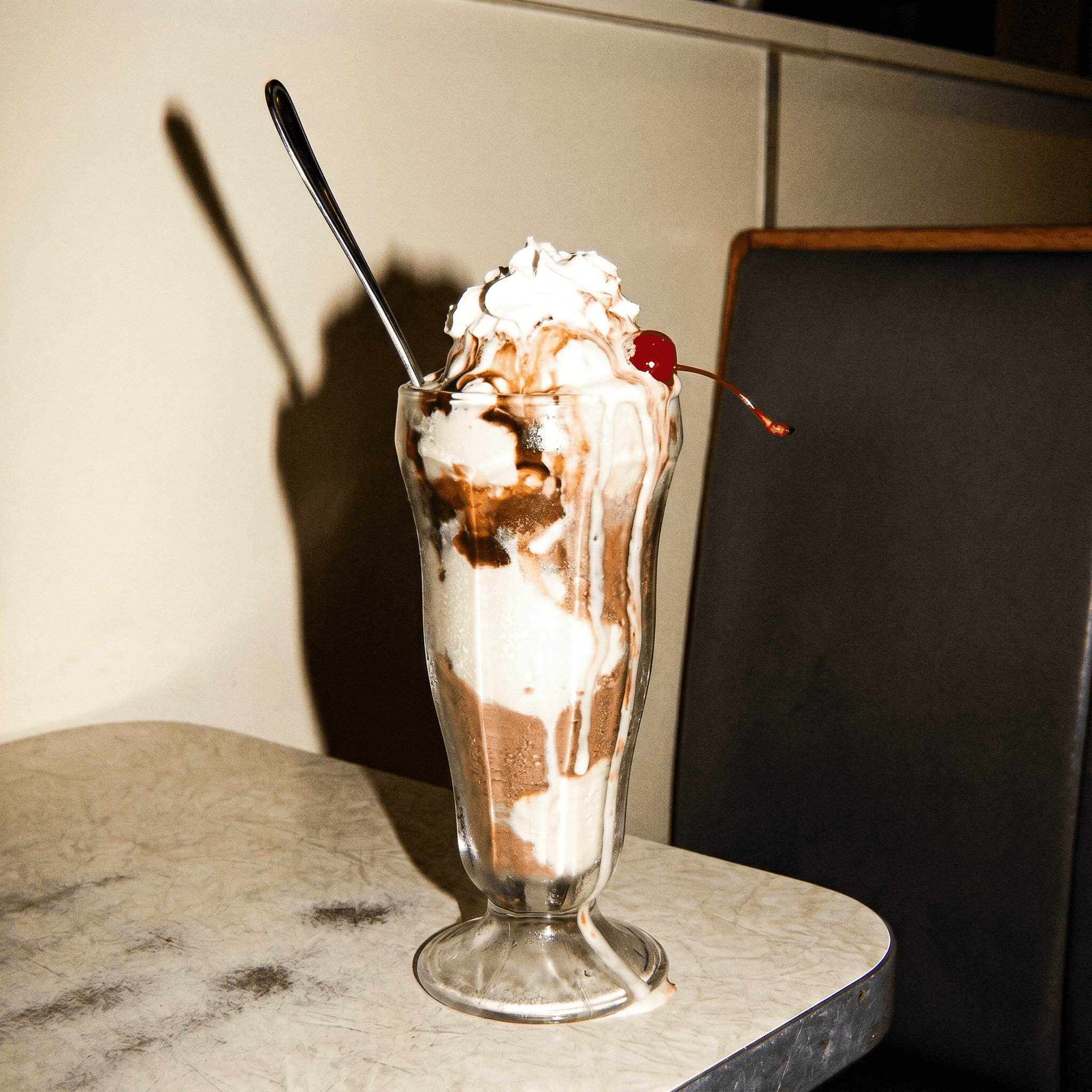 An ice-cream sundae melting fast in a tall glass, drips on the counter, frozen by camera flash.