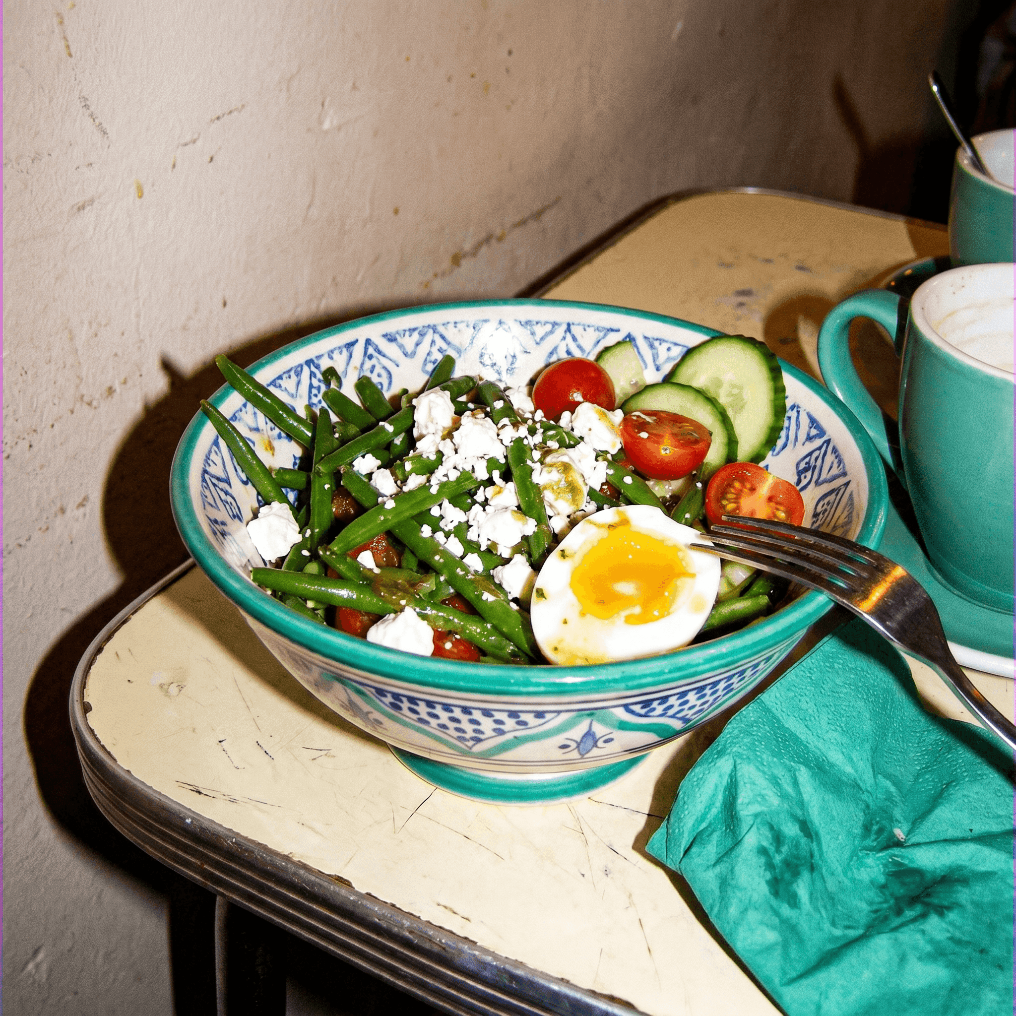 A big vivid salad in a blue-and-white bowl on a market counter, colours blown out by direct flash.