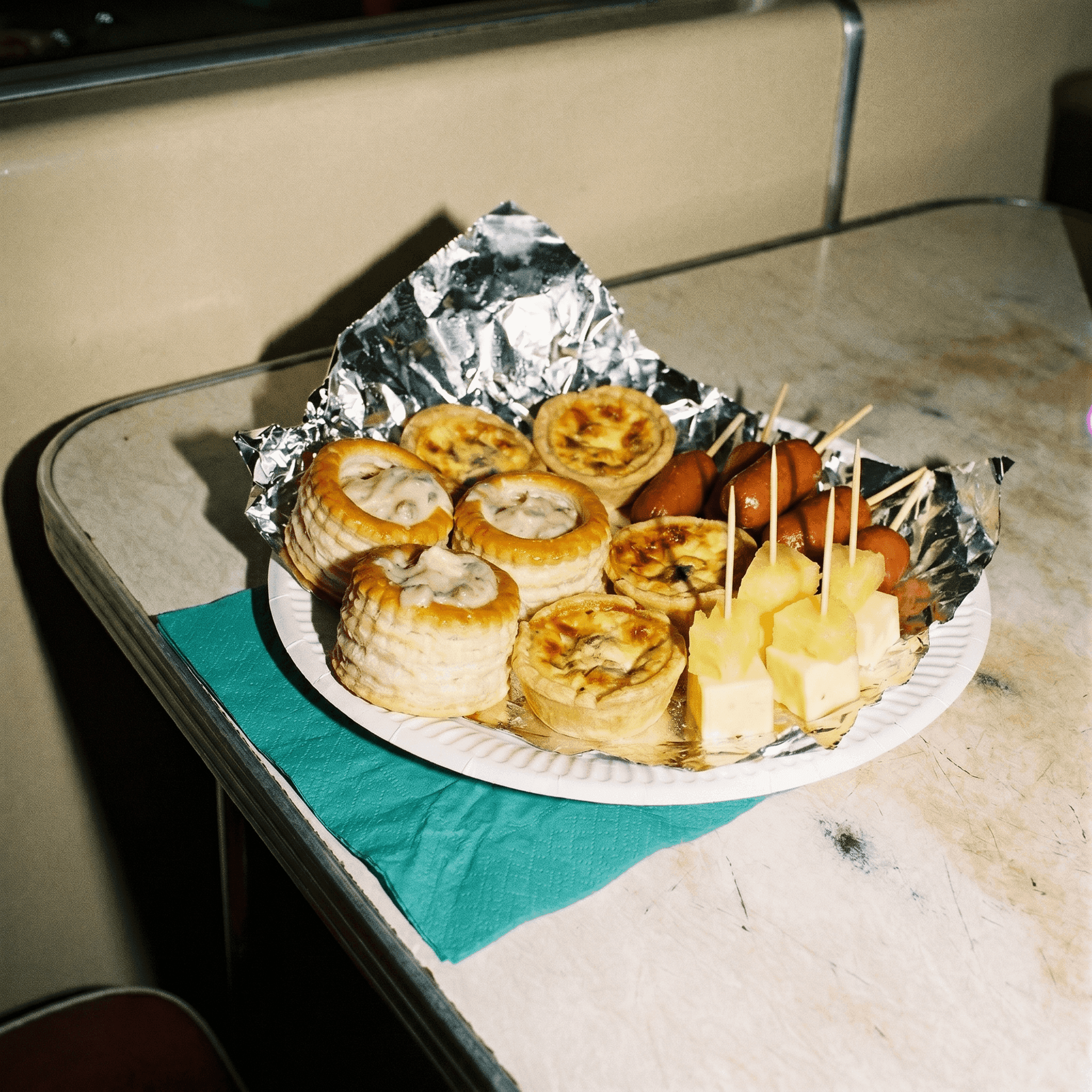An early-2000s party buffet plate of pastry vol-au-vents, mini quiches and cocktail sausages, shot with bright flash.